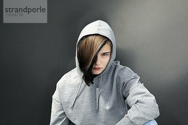 Teenage girl wearing hooded shirt against gray background