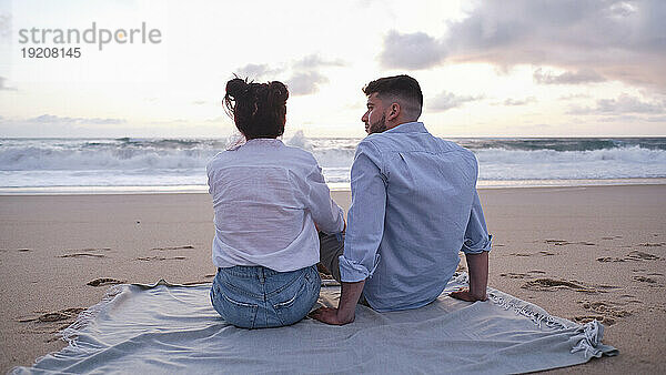 Freund und Freundin sitzen auf einer Decke am Strand
