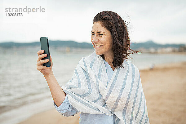 Lächelnde Frau  die am Strand ein Selfie mit ihrem Smartphone macht