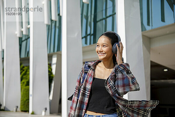 Smiling student listening to music near university