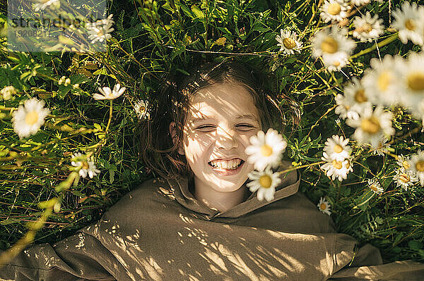 Smiling boy lying amidst daisies in field