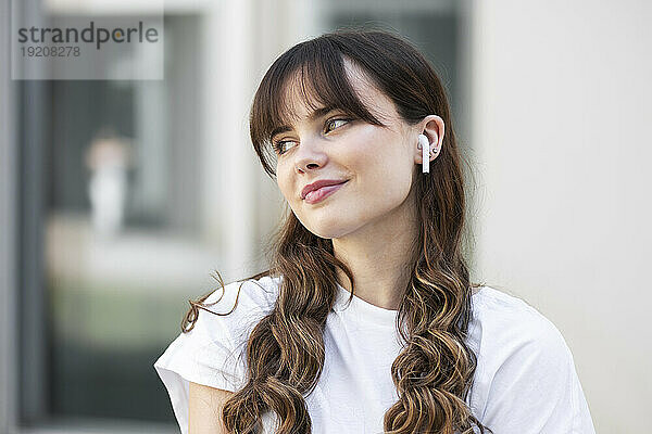 Lächelnde junge Frau mit kabellosen In-Ear-Kopfhörern  die Musik hört