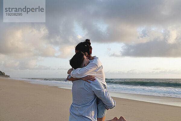 Junger Mann hebt Freundin am Strand auf den Arm