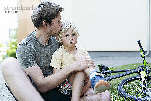 Vater küsst und kümmert sich um Sohn  der vom Fahrrad gefallen ist