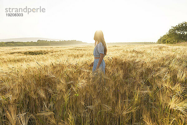 Mädchen steht an einem sonnigen Tag inmitten der Weizenernte auf dem Feld