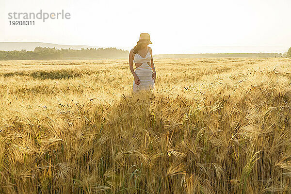 Frau mit Hut steht inmitten der Weizenernte im Feld