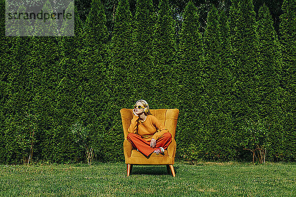 Blonde Frau sitzt auf einem Sessel im Garten