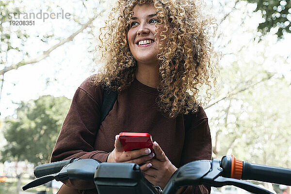 Nachdenkliche junge Frau hält Smartphone am Fahrrad