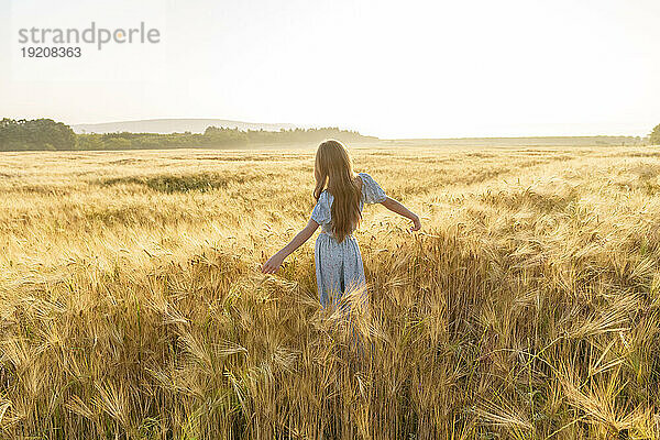 Mädchen mit ausgestreckten Armen steht inmitten der Weizenernte im Feld