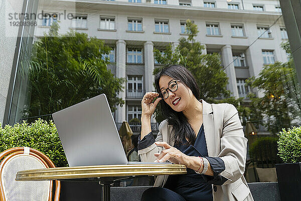 Lächelnde Geschäftsfrau arbeitet mit Laptop im Straßencafé