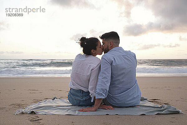 Affectionate couple kissing each other sitting on sand at beach