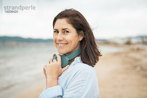 Glückliche Frau mit kabellosen Kopfhörern am Strand