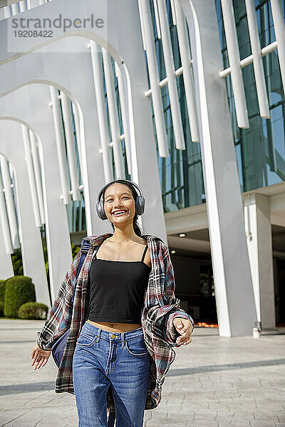 Fröhlicher Student  der Musik hört und vor dem Universitätsgebäude läuft