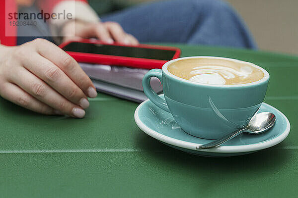 Frau mit Kaffeetasse und Smartphone am Tisch