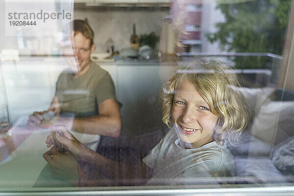 Lächelnder Vater und Sohn schauen aus der Küche durch das Fenster