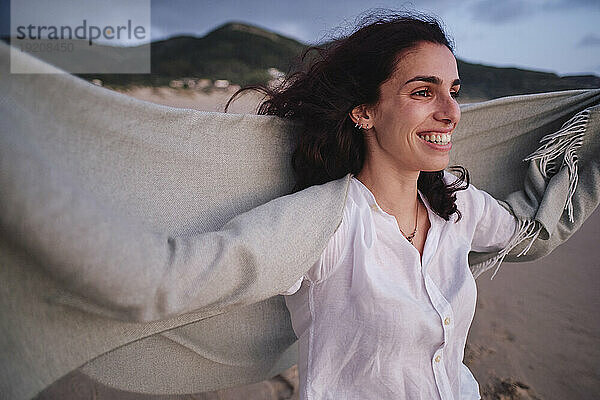 Happy woman holding blanket at beach