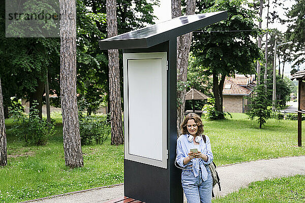 Frau benutzt Mobiltelefon und stützt sich auf Solarladestation im Park