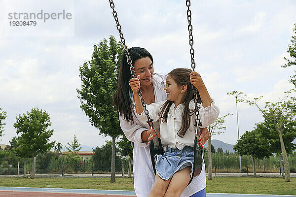 Glückliche Mutter verbringt Zeit mit ihrer Tochter  die auf der Schaukel im Park sitzt