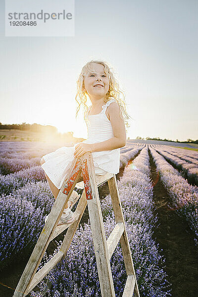 Thoughtful girl sitting on wooden step ladder in field