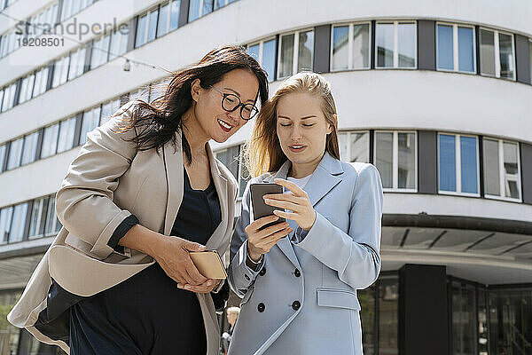 Geschäftsfrau teilt Smartphone mit Kollegin vor Gebäude