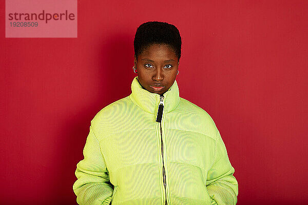 Woman wearing green jacket standing against red background