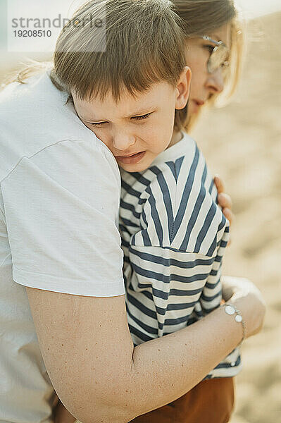 Mutter umarmt traurigen Sohn am Strand