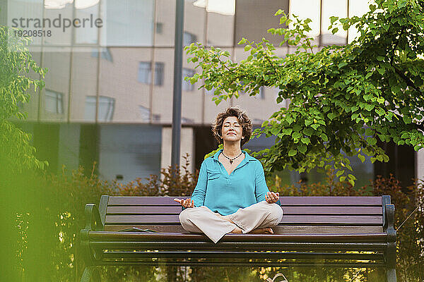 Lächelnde Geschäftsfrau meditiert auf Parkbank