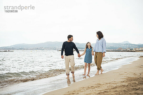 Glücklicher Mann und Frau mit Tochter  die am Strand spazieren gehen