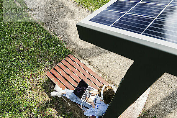Frau sitzt mit Laptop unter Solarladestation im Park