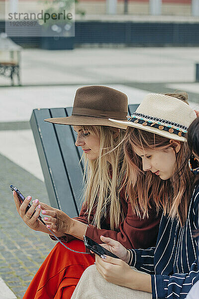 Mutter und Tochter benutzen Smartphone auf Bank