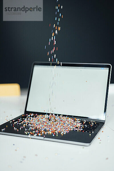 Mehrfarbige Perlen fallen auf Laptop am Schreibtisch
