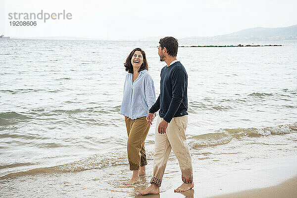 Fröhliches Paar hält Händchen und geht am Strand spazieren