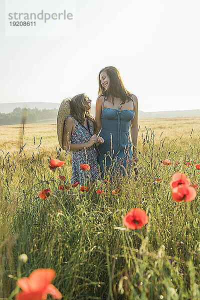 Lächelnde Mutter und Tochter verbringen ihre Freizeit im Mohnfeld