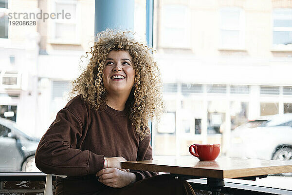Junge Frau mit lockigem Haar sitzt am Tisch im Café