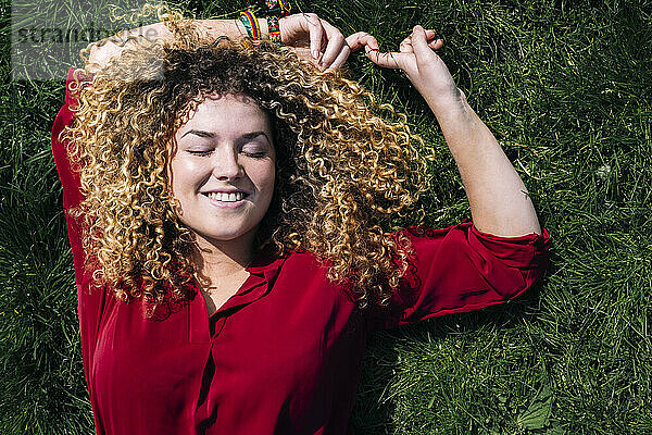 Lächelnde Frau mit lockigem Haar  die im Gras liegt