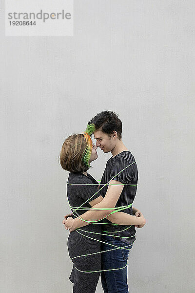 Teenage couple tied up with rope embracing each other against gray background
