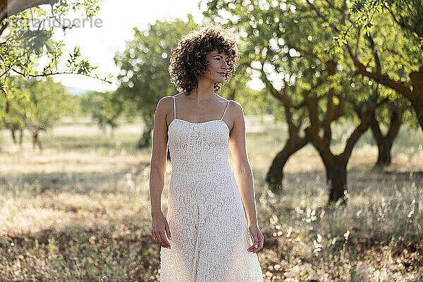 Woman with curly hair walking in front of trees at sunny day
