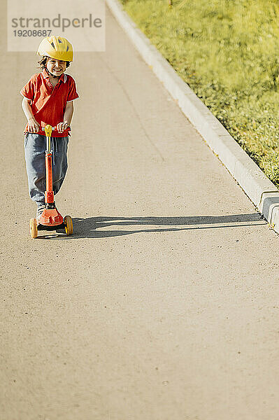 Lächelnder Junge fährt Tretroller auf Fußweg