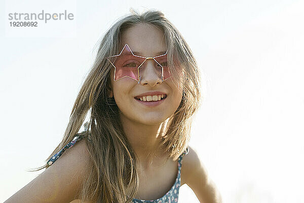 Smiling girl wearing star shaped sunglasses in front of sky