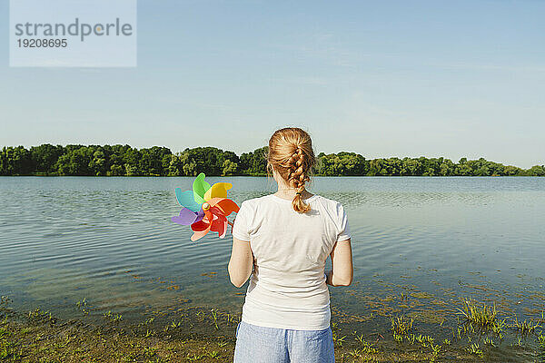 Frau hält Regenbogen-Windradspielzeug am Seeufer