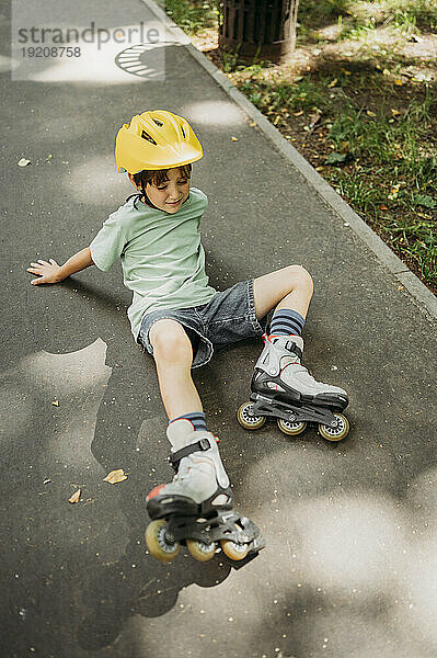 Verärgerter Junge mit Inline-Skates liegt auf Fußweg