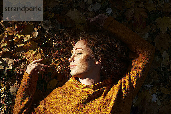 Rothaarige Frau schläft auf Herbstblättern im Park