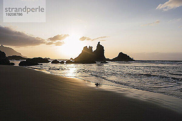 Silhouette von Wellen und Felsen am Strand bei Sonnenuntergang