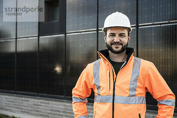 Lächelnder  selbstbewusster Ingenieur  der vor Solarpaneelen steht