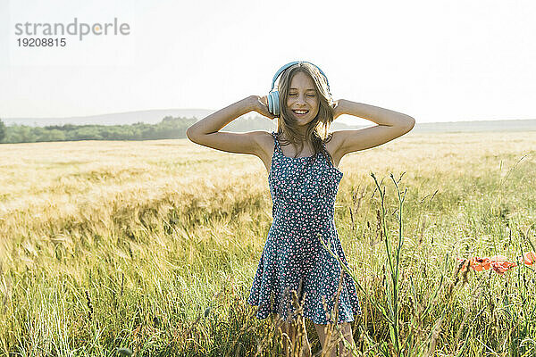 Happy girl enjoying music with wireless headphones in poppy field