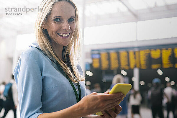 Lächelnde Geschäftsfrau steht mit Smartphone