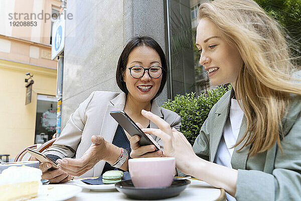 Happy business partners discussing with smart phones sitting at sidewalk cafe