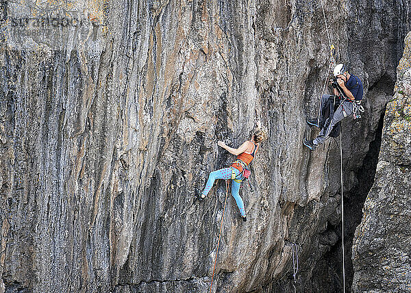 Mann fotografiert Frau beim Bergsteigen mit Seil
