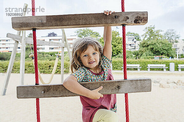 Playful girl climbing ladder at beach
