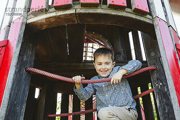 Lächelnder Junge sitzt auf Spielgeräten im Freien auf dem Spielplatz